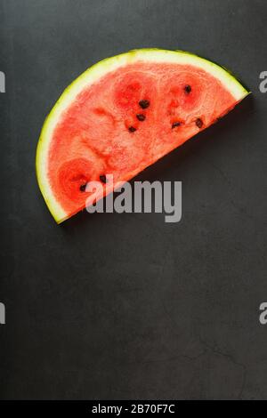 Saftige Scheibe roter Wassermelone auf steinschwarzem Grund. Konzeptionelle Farben des Sommers. Draufsicht als Hintergrund Stockfoto