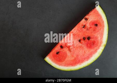 Saftige Scheibe roter Wassermelone auf steinschwarzem Grund. Konzeptionelle Farben des Sommers. Draufsicht als Hintergrund Stockfoto