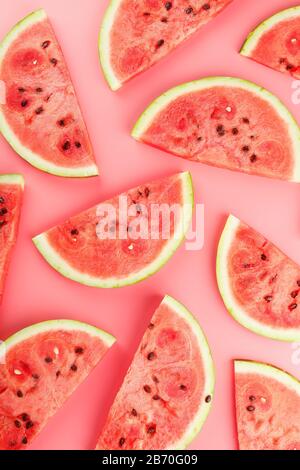 Saftige Scheiben roter Wassermelone auf hellrosa Hintergrund. Konzeptionelle Farben des Sommers. Muster in der Draufsicht als Hintergrund oder Substrat Stockfoto