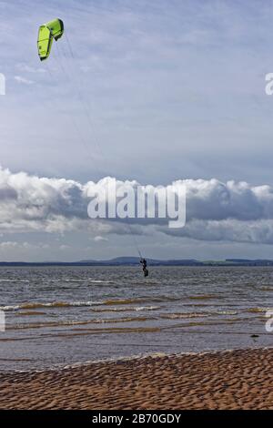 Ein Kite Surfer in einem Wetsuit, der die Windy Conditions in der Tay Estuary verwendet, um mit seiner Kite vom Wasser zu springen. Stockfoto