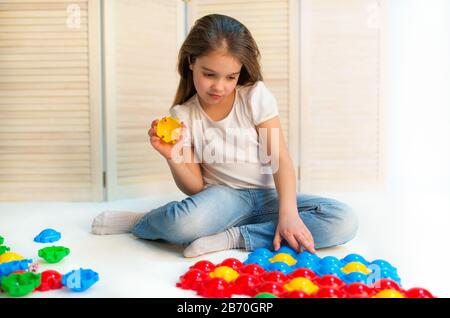 Kleines neugieriges Mädchen legt Plastikrätsel auf den Boden, das in ihrem Kinderzimmer sitzt. Entwicklungskonzept für die frühe Kindheit Stockfoto