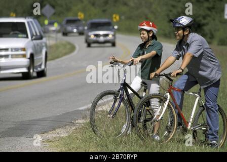 Austin Texas USA: Das 13-jährige hispanische Mädchen und der junge Mann warten darauf, eine befahrene Straße mit dem Fahrrad zu überqueren. HERR ©Bob Daemmrich Stockfoto