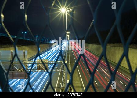 Nachts führt eine Autofahrt auf einer Autobahn in den Niederlanden durch. Blick von hinter einem Metallzaun. Selektiver Fokus. Stockfoto