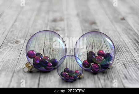 Drei schöne transparente Kugeln mit kleinen rosa und violetten Kugeln im Inneren auf Holzboden Stockfoto