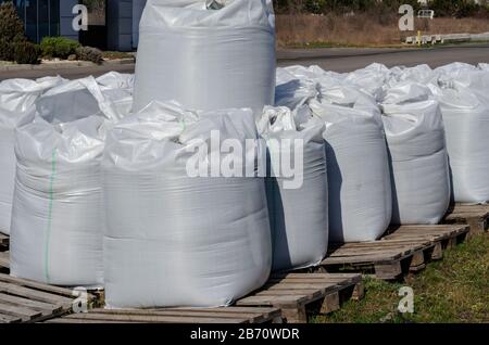 Stückgut in Großbeuteln. Weiße Big Bags auf Holzpaletten im Freien. Eine Lieferung wartet auf das Laden. Umschlag und Logistik. Seitenansicht. Se Stockfoto