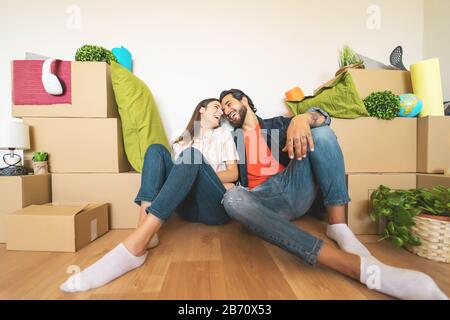 Glückliches junges Paar, das zum ersten Mal nach Hause zieht - Mann und Frau haben Spaß beim Auspacken der Kartonschachtel im neuen Haus Stockfoto