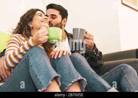 Junges Paar trinkt Kaffeetasse auf dem Boden neben dem Sofa - glückliche Liebhaber haben zu Hause zarte Momente zusammen Stockfoto