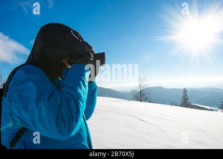 Junger Reisender mit Rucksack fotografiert in einem hohen, schneebedeckten Tannenbaum in hoher Schneeverwehung vor dem Hintergrund von Nebel auf einem frostigen Winter d Stockfoto