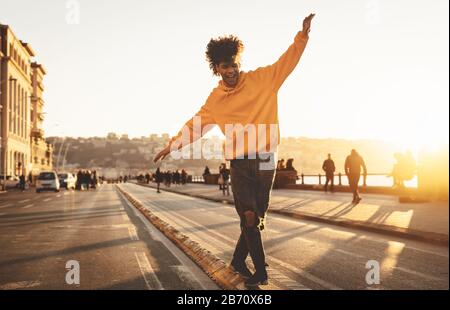 Afro American man hat Spaß beim gehen im Stadtzentrum - fröhlicher junger Kerl, der Zeit für einen Sonnenuntergang im Freien genießt Stockfoto