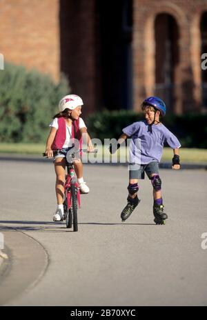 Austin, Texas, USA: Das Kind fährt Fahrrad, während ihre Freundin in einem bürgerlichen Viertel mit Rollerblättern unterwegs ist. ©Bob Daemmrich Stockfoto