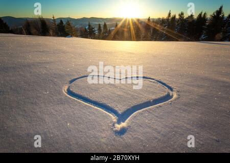 Herz trampelte auf dem Schnee mit Füßen in einer Schneeverwehung auf einem Hang mit herrlichem Blick auf den Nadelwald und die Bergketten auf einem sonnigen Frost Stockfoto