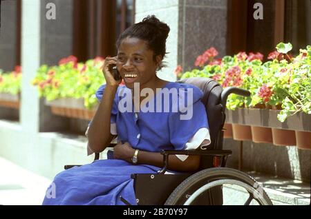 Austin Texas USA: Behinderte Frau im Rollstuhl nutzt ein Handy auf dem Bürgersteig der Stadt. ©Bob Daemmrich Stockfoto