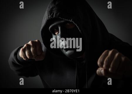 Studioaufnahme von unerkennbarem Kapuzenmann mit schwarzer Maske und geklatschten Fäusten Stockfoto