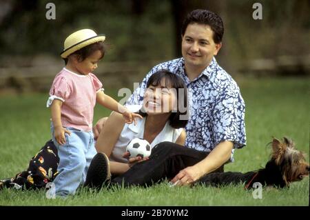 Austin, Texas, USA, 1995: Hispanischer Vater und philippinisch-amerikanische Mutter mit zweijähriger Tochter und Familienhund, die im Park spielen. HERR ©Bob Daemmrich Stockfoto