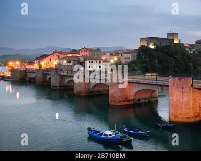 Zeitliches Bild der Brücke La Barquera und des beleuchteten Dorfes und Schlosses, San Vicente de La Barquera, Kantabrien, Spanien Stockfoto