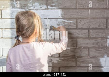 Der Maler, der Pflaster malt eine Wand. Abschluss der Fassaden mit Backstein. Bau- und Reparaturarbeiten. Ziegelwerk. Ein kleines Mädchen wird einen Stein malen w Stockfoto