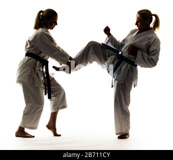 Zwei Mädchen in weißen Kimonos mit schwarzen und blauen Bändern, Training und Üben von Karate-Ständen und Techniken Stockfoto