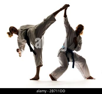 Zwei Mädchen in weißen Kimonos mit schwarzen und blauen Bändern, Training und Üben von Karate-Ständen und Techniken Stockfoto