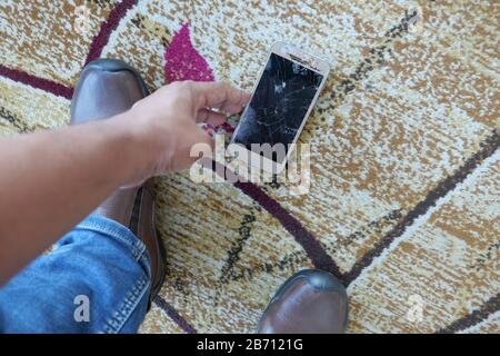 Mann Handpflücken zerbrochenes Smartphone vom Boden Stockfoto