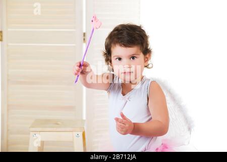 Kleines Mädchen mit großen braunen Augen, bekleidet in Feenkostüm, Hand erhoben und hält Zauberstab Stockfoto