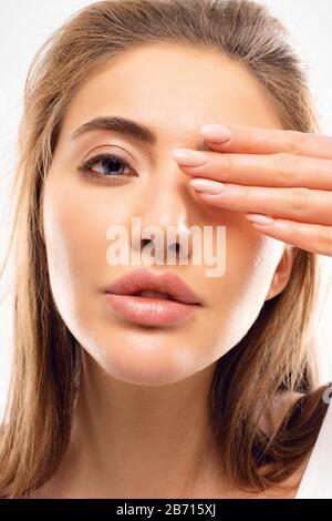 Eine junge, elegante Dame mit großen Lippen und zart glatter Haut versteckt das Auge unter schlanken Fingern mit Maniküre. Kümmert sich um ihre Haut, nimmt Spa-Verfahren und Stockfoto