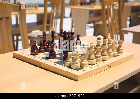 Gelbes und braunes Foto mit einem Bild von Schachbrettstücken, Holzstücken auf einem Schachbrett und Emtytisch . So spielen Sie Holzschach. Schach Stockfoto
