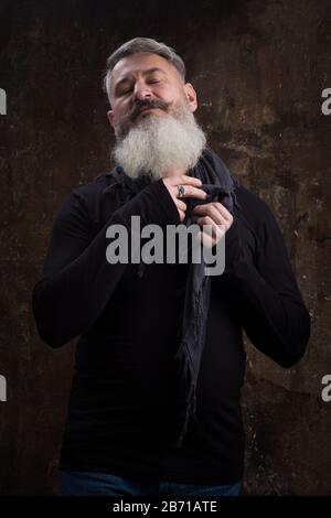Studio-Porträt eines gutaussehenden, fälligen grauhaarigen bärtigen Mannes gegen die dunkle Wand, selektiver Fokus Stockfoto