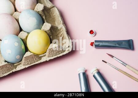 Das Konzept, Ostereier in pastellfarbenen Wasserfarben zu färben. Farben und Bürsten zum Färben von Eiern für Ostern auf pinkfarbenem Hintergrund. Stockfoto