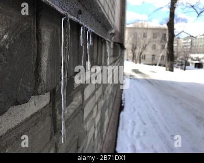 Eiszapfen hängen am Visier eines grauen Gebäudes neben der Straße, Quelltauchung Stockfoto