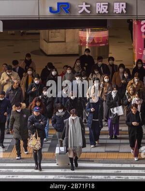 Osaka, Japan - 4. März 2020: Eine kleine Menschenmenge von meist maskierten Fußgängern überquert die Straße unter der Beschilderung zum Bahnhof JR Osaka Stockfoto