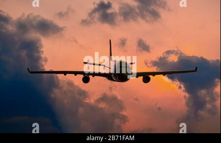 Silhouette eines kommerziellen Flugzeuges, der über dramatischen Wolken in wunderschönem Sonnenuntergang fliegt. Reisekonzept. Stockfoto