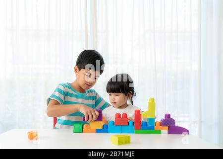 Süßer asiatischer Bruder und Schwester spielen mit einem Spielzeugblockdesigner auf dem Tisch im Wohnzimmer zu Hause. Konzept der Bindung von Geschwistern, Freundschaft und Lernen Stockfoto