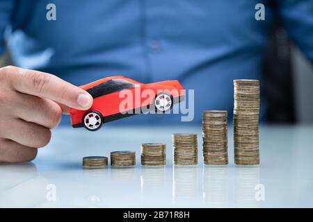 Person, Die Red Car Über Steigende Gestapelte Münzen Hält Stockfoto