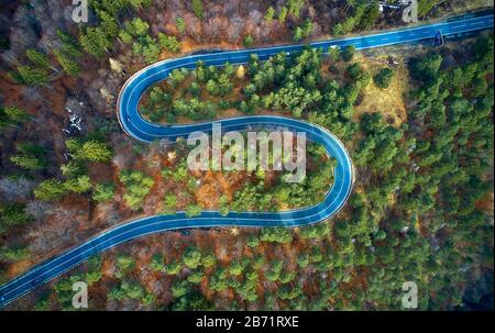 Der Luftbild der kurvenreichen Straße vom hohen Gebirgspass mit Bäumen in Siebenbürgen, Rumänien, in der Herbst-Winter-Zeit geschwungene Straßenansicht per Drohne Stockfoto