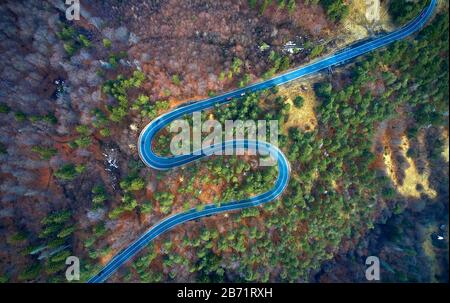 Der Luftbild der kurvenreichen Straße vom hohen Gebirgspass mit Bäumen in Siebenbürgen, Rumänien, in der Herbst-Winter-Zeit geschwungene Straßenansicht per Drohne Stockfoto