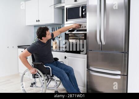 Behindertengerechter Mann Mit Mikrowellenofen Zum Backen In Der Küche Stockfoto