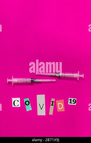 Anordnung von zwei medizinischen Spritzen und COVID-19-Beschriftung. Seine Briefe werden aus einem Magazinpapier geschnitten und auf pinkfarbenem Hintergrund zusammengefügt Stockfoto