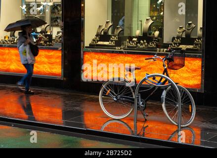 Eine junge Frau spaziert mit einem Regenschirm entlang der Straße in Melbourne Australia, Schaufenster, das sich auf dem nassen Fußweg widerspiegelt. Stockfoto