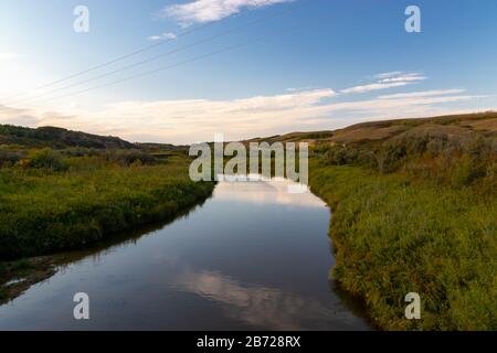 Ein ruhiger und friedlicher Bach, der durch ein Tal im ländlichen Teil der Saskatchewan Prairies in Kanada fließt und der Himmel im Wasser reflektiert Stockfoto