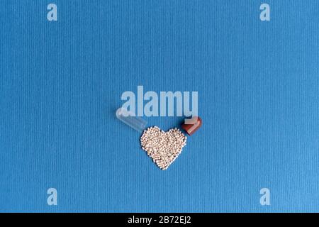 Granulat aus einer herzförmigen Kapsel auf klassischem blauem Grund gegossen. Herzförmige Medikamente. Herzsymbol durch Pillen gezeichnet. Stockfoto