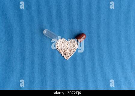 Granulat aus einer herzförmigen Kapsel auf klassischem blauem Grund gegossen. Herzförmige Medikamente. Herzsymbol durch Pillen gezeichnet. Stockfoto