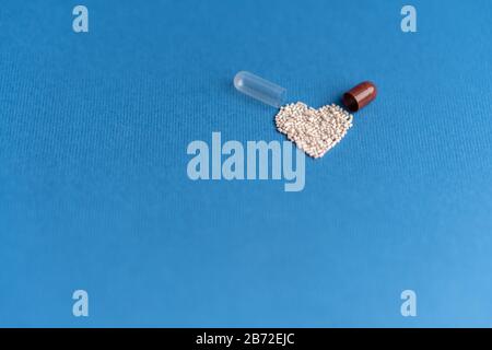Granulat aus einer herzförmigen Kapsel auf klassischem blauem Grund gegossen. Herzförmige Medikamente. Herzsymbol durch Pillen gezeichnet. Stockfoto