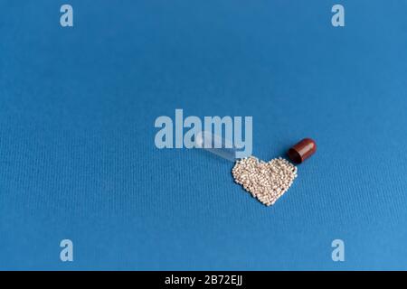 Granulat aus einer herzförmigen Kapsel auf klassischem blauem Grund gegossen. Herzförmige Medikamente. Herzsymbol durch Pillen gezeichnet. Stockfoto