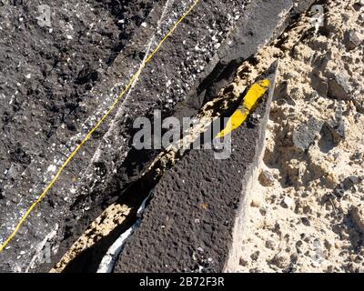 Asphaltrückstände auf der Straße, Nahbereich der zerbrochenen Asphaltpflasteroberfläche mit Fragment der bemalten gelben Linie, Asphaltschutt, Asphaltschutt und Asphaltschutt Stockfoto