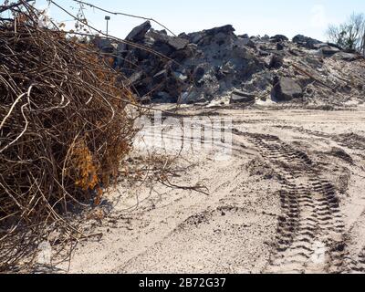 Schwere Ausrüstung Reifenspuren am Road Demolition Site, Haufen toter Sträucher, Äste, Wurzeln, im Hintergrund riesiger Stapel aus Beton und Asphalt Ansicht #1 Stockfoto