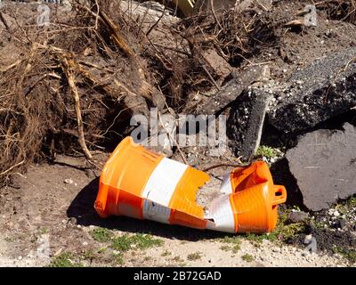 Trümmerhaufen von Straßenvernichtung, Abriss, Umweltunfall: Tote Bäume, Sträucher, verdorrte Wurzeln, zerdrückter orangefarbener Warnkegel, Asphalt Stockfoto