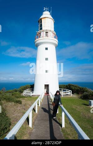 Blick auf den Cape Otway Lighthouse in Victoria, Australien als weibliche Touristin, posiert humorvoll auf die Leitplanken, die direkt zur Tür führen. Stockfoto