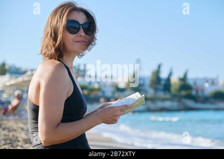 Sommerfrau sitzt auf Sandufer Lesebuch, sonnt sich in untergehenden Sonne Stockfoto
