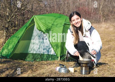 Fröhliche Frau, die allein vor ihrem Zelt kochte und Zeit für draußen hatte Stockfoto