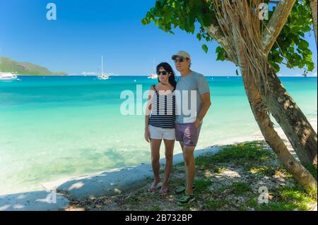 Ein Paar, das sich unter einem Baum umarmt und einen Strand auf dem Fitzroy Island Resort in Queensland, Australien, hinunterblickt. Stockfoto